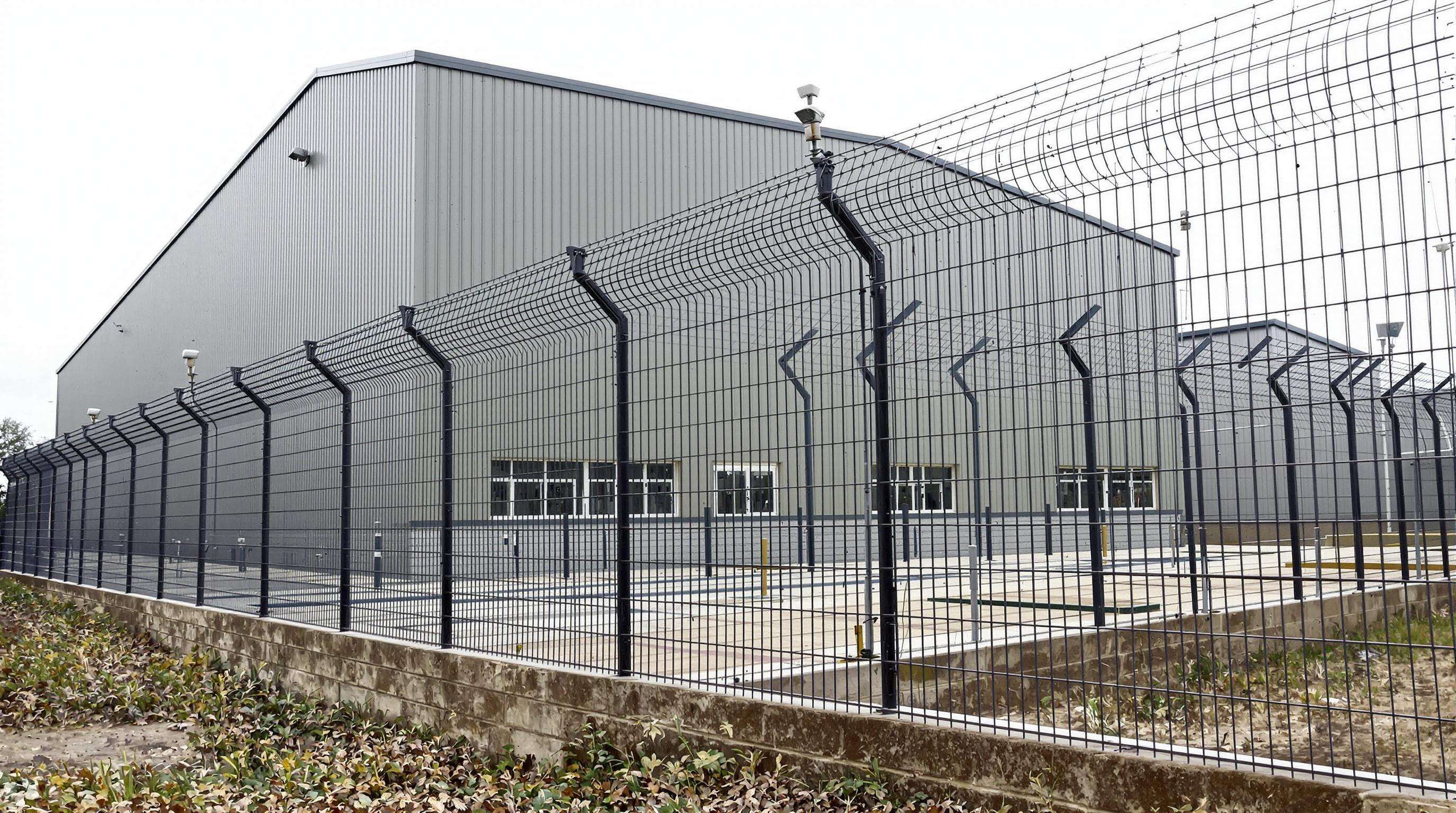 Modern prefab warehouse secured by tall steel mesh fencing and surveillance cameras