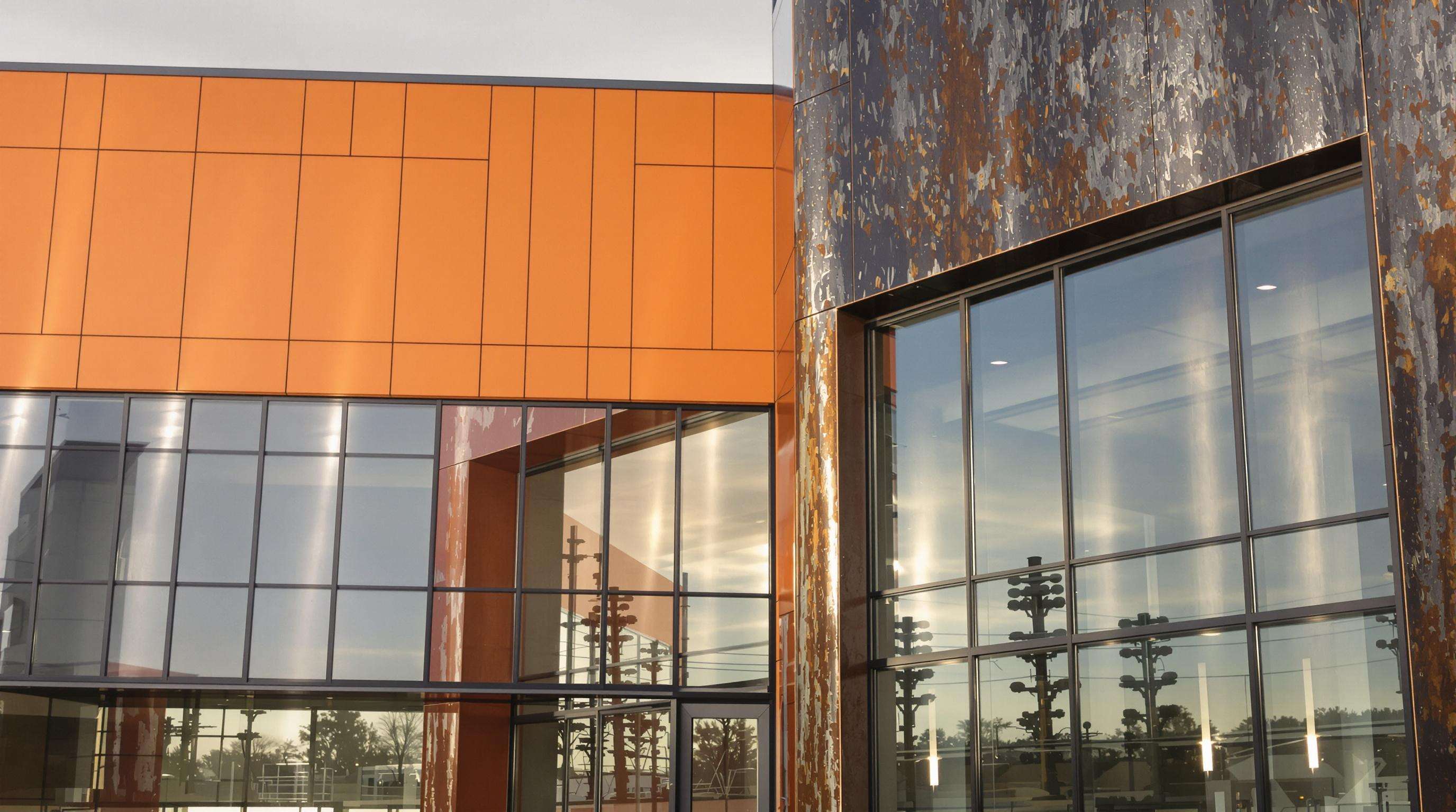 Modern steel building facade featuring bold colored panels, rust textures, glass, and wavy metallic cladding in dramatic early morning light