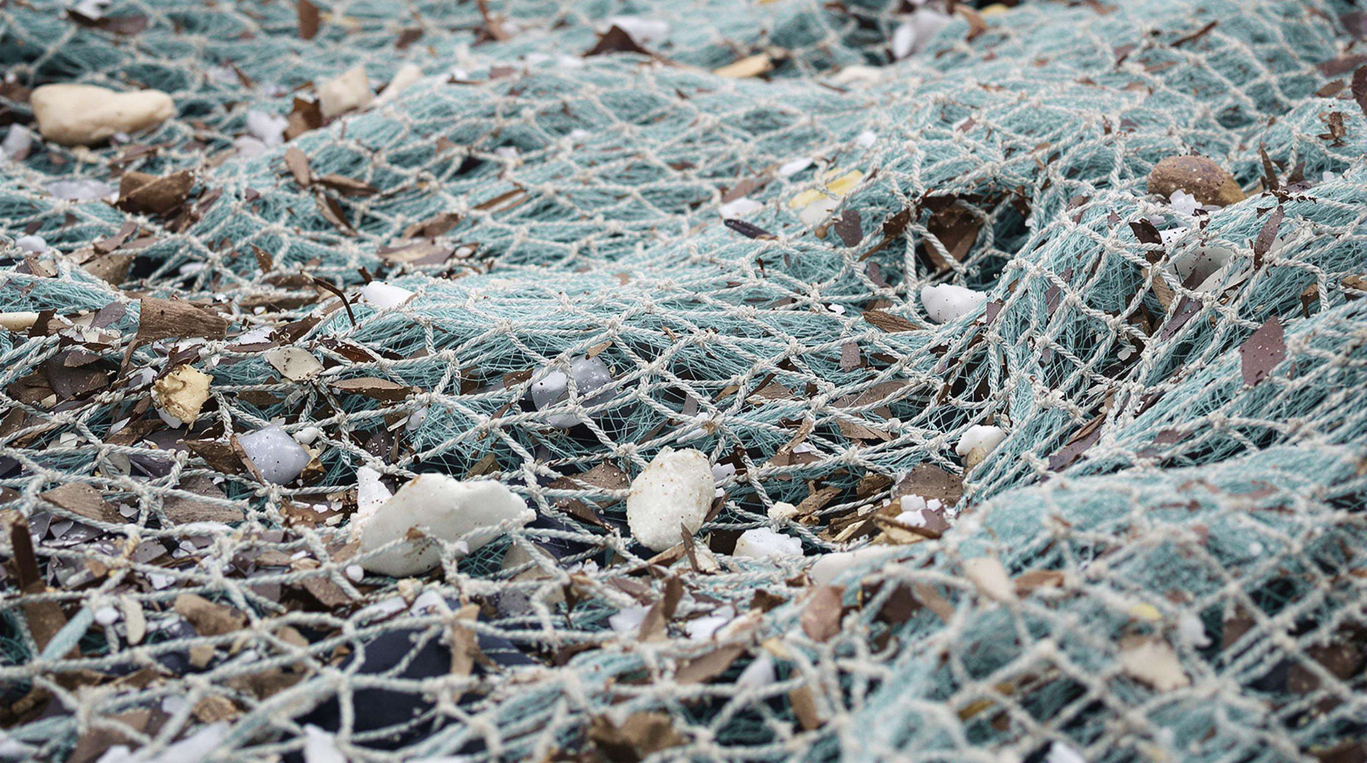 Close-up view of a debris-laden safety net at a construction site, showing dust, sharp debris, and water-soaked patches stressing the fibers.