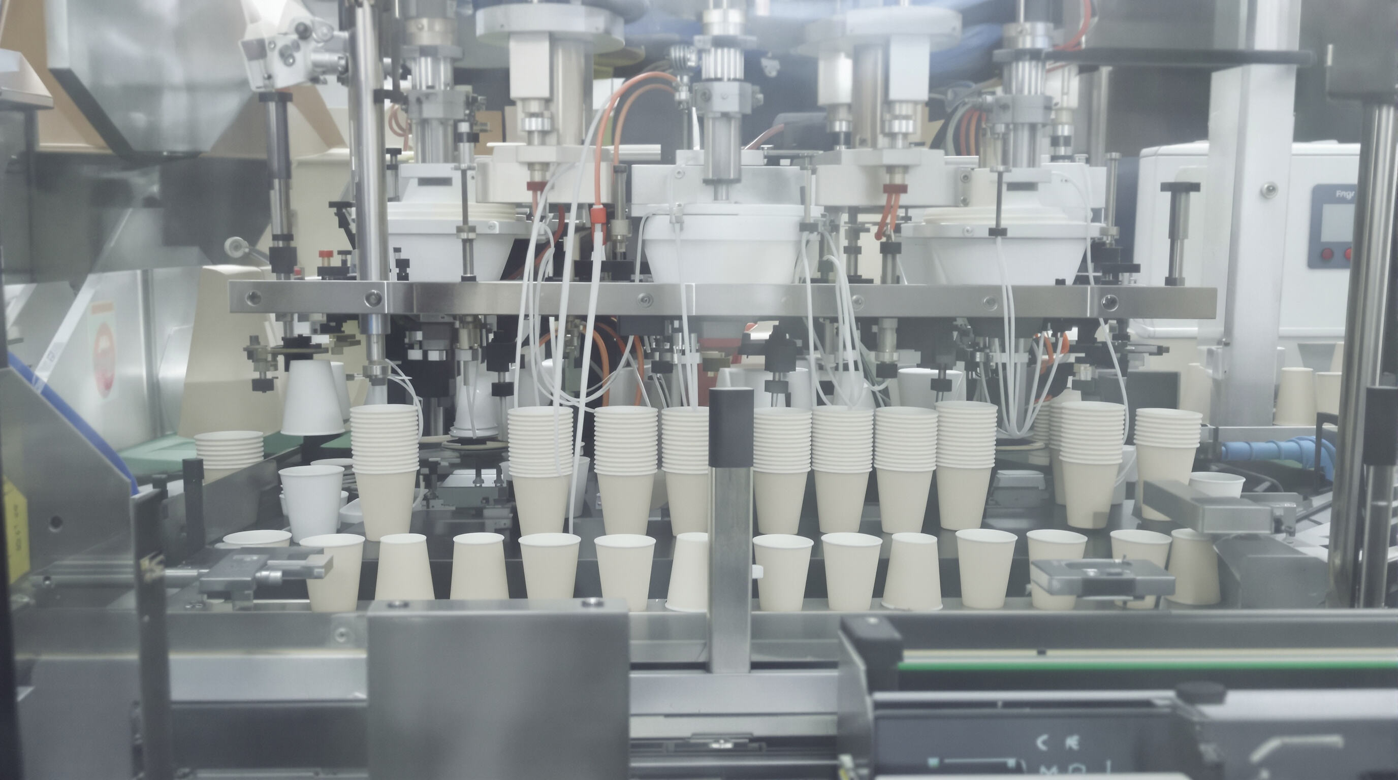 Photorealistic view of an industrial paper cup machine in operation showing key mechanical stages and finished cups.