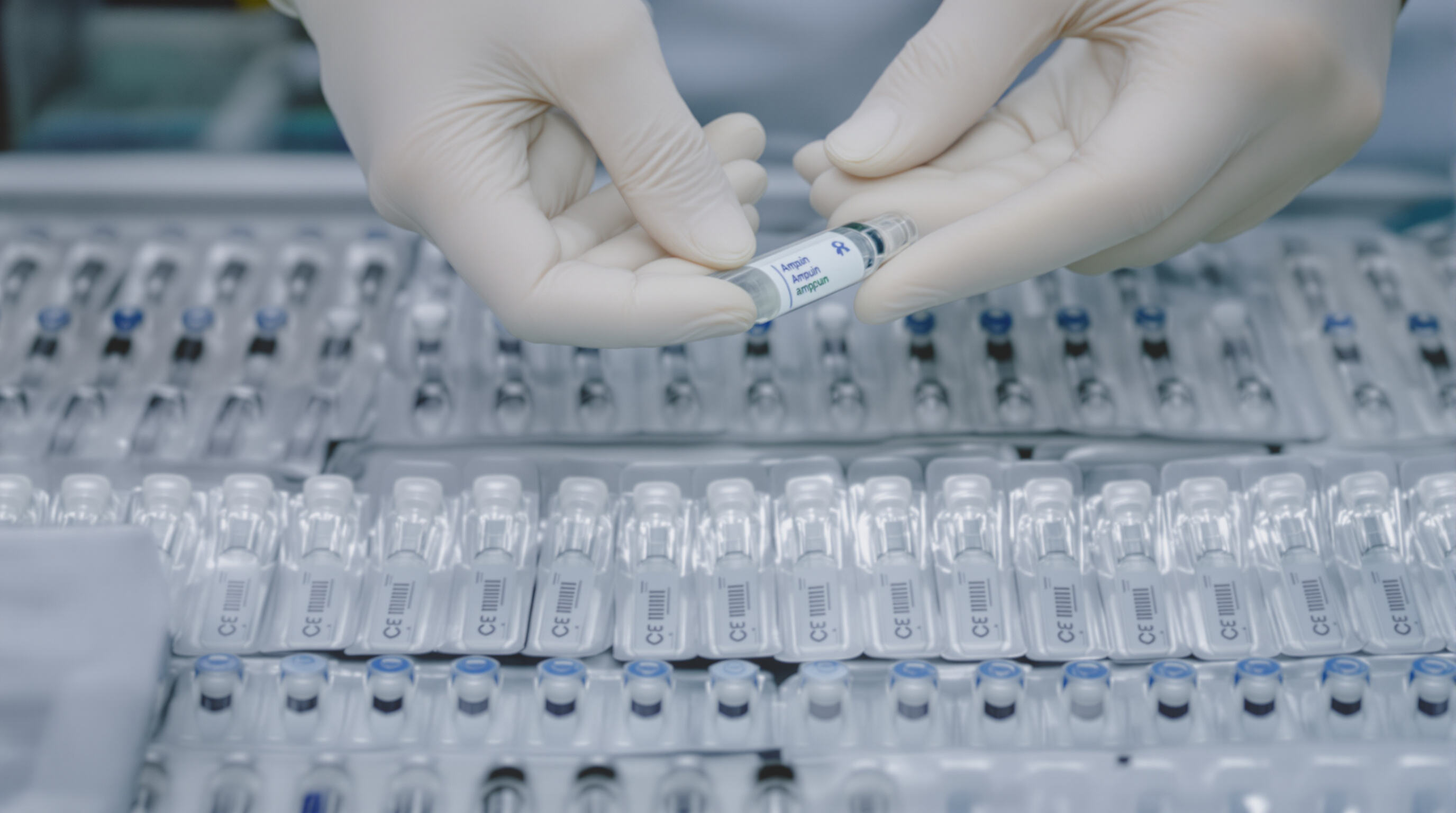Close-up of hands handling a single-use ampoule serum with more ampoules in sterile packaging