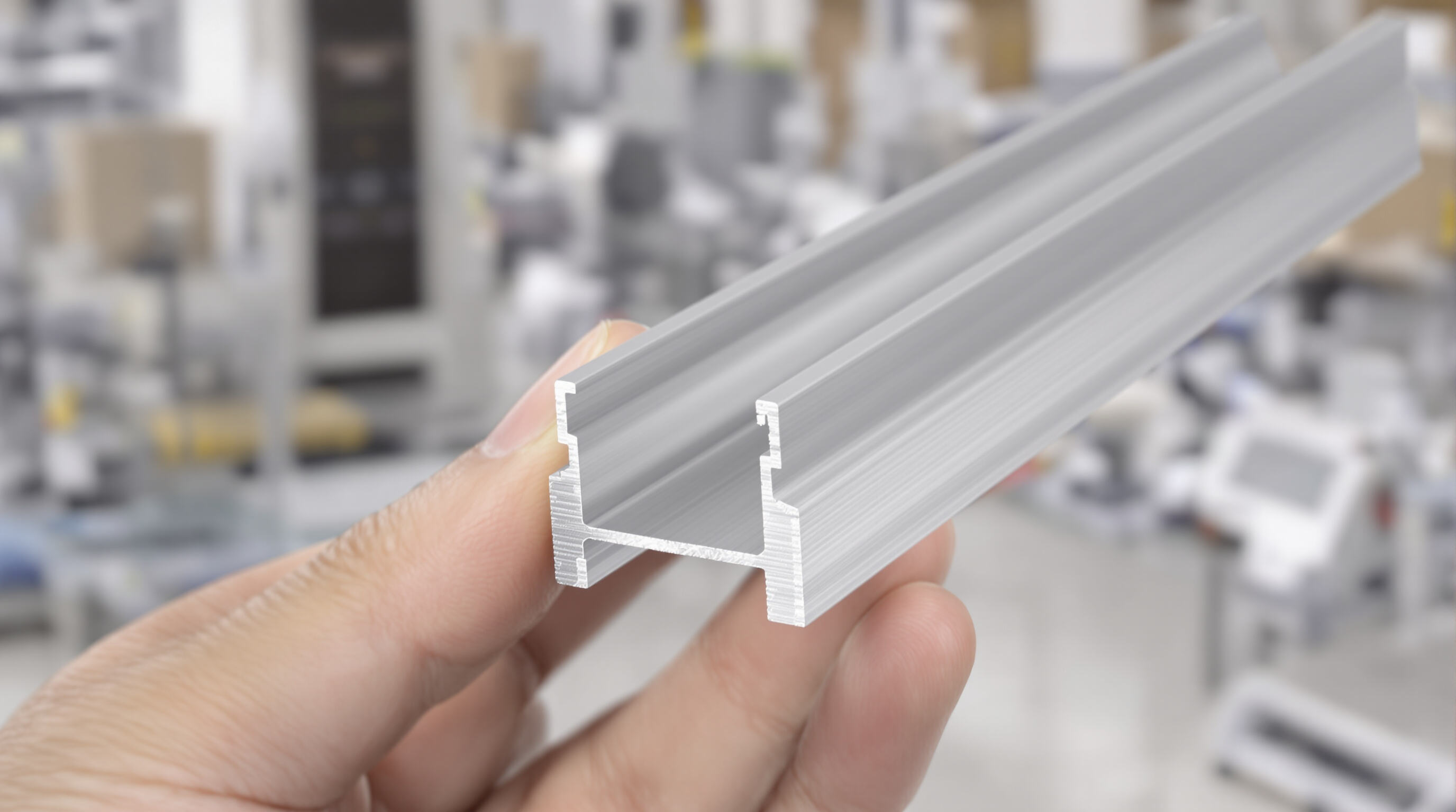 A close-up photo of a hand holding a silver aluminum extrusion, highlighting material texture and industrial setting.