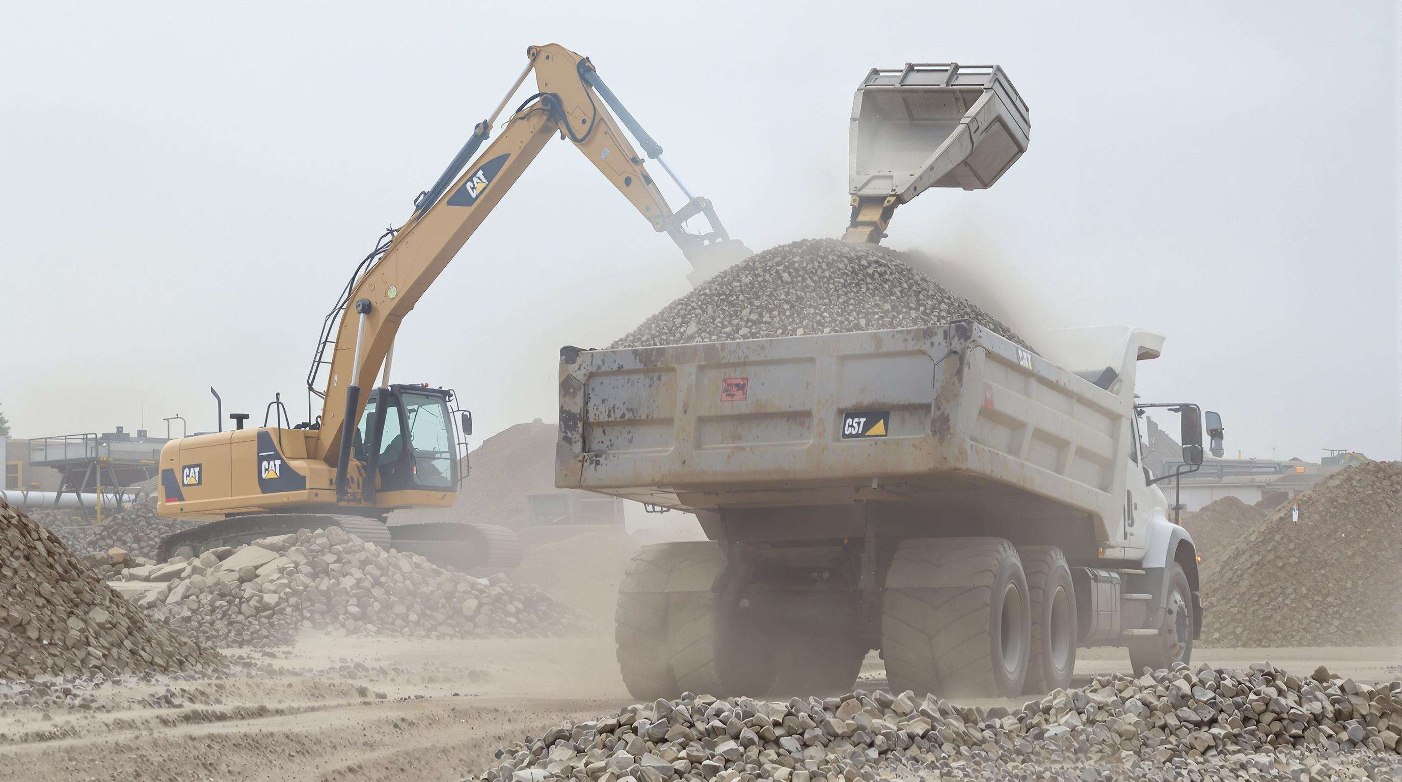 Dump truck being loaded with gravel at a job site with focus on payload and engine
