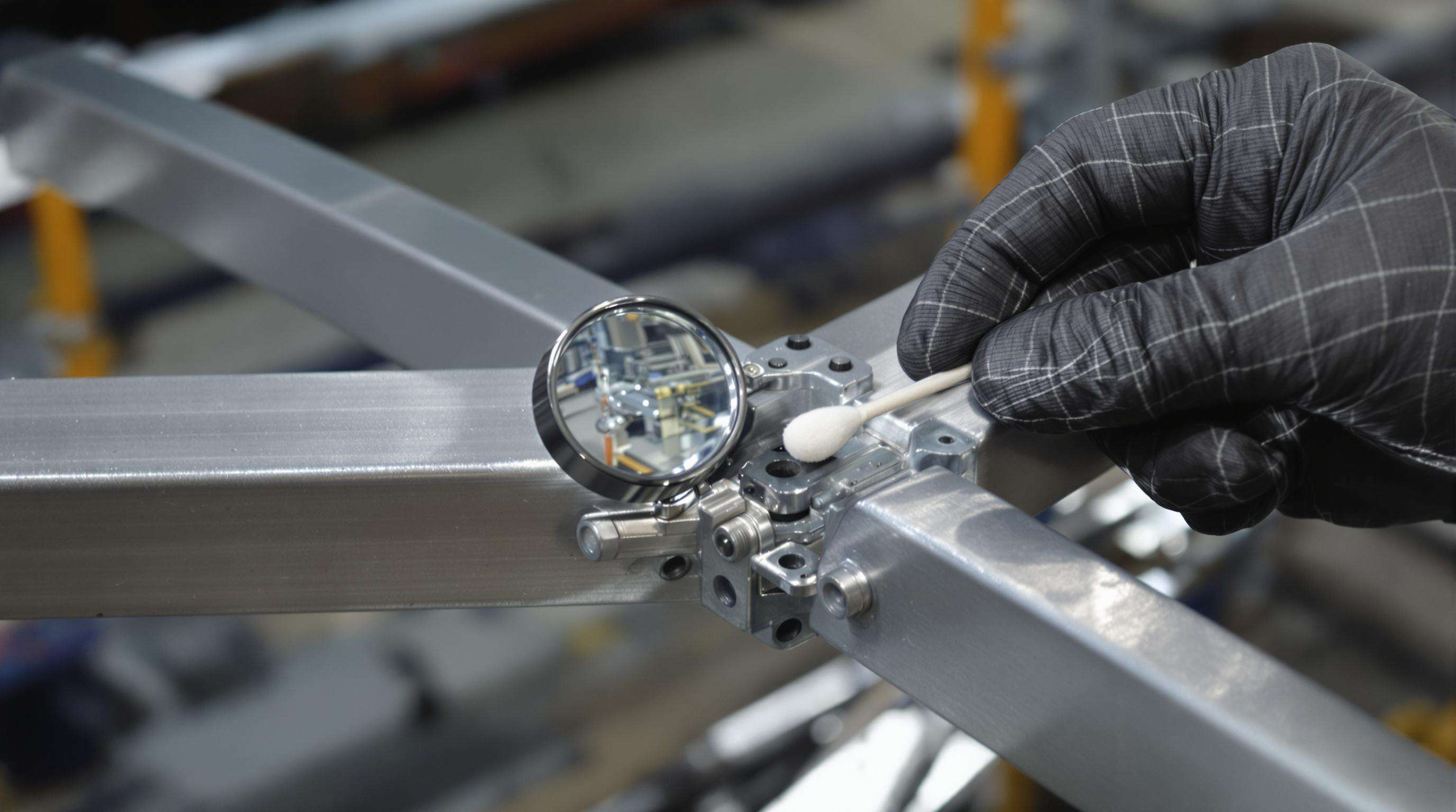 Technician closely inspecting an aluminum truss joint for micro-cracks using a magnifier and cotton swab