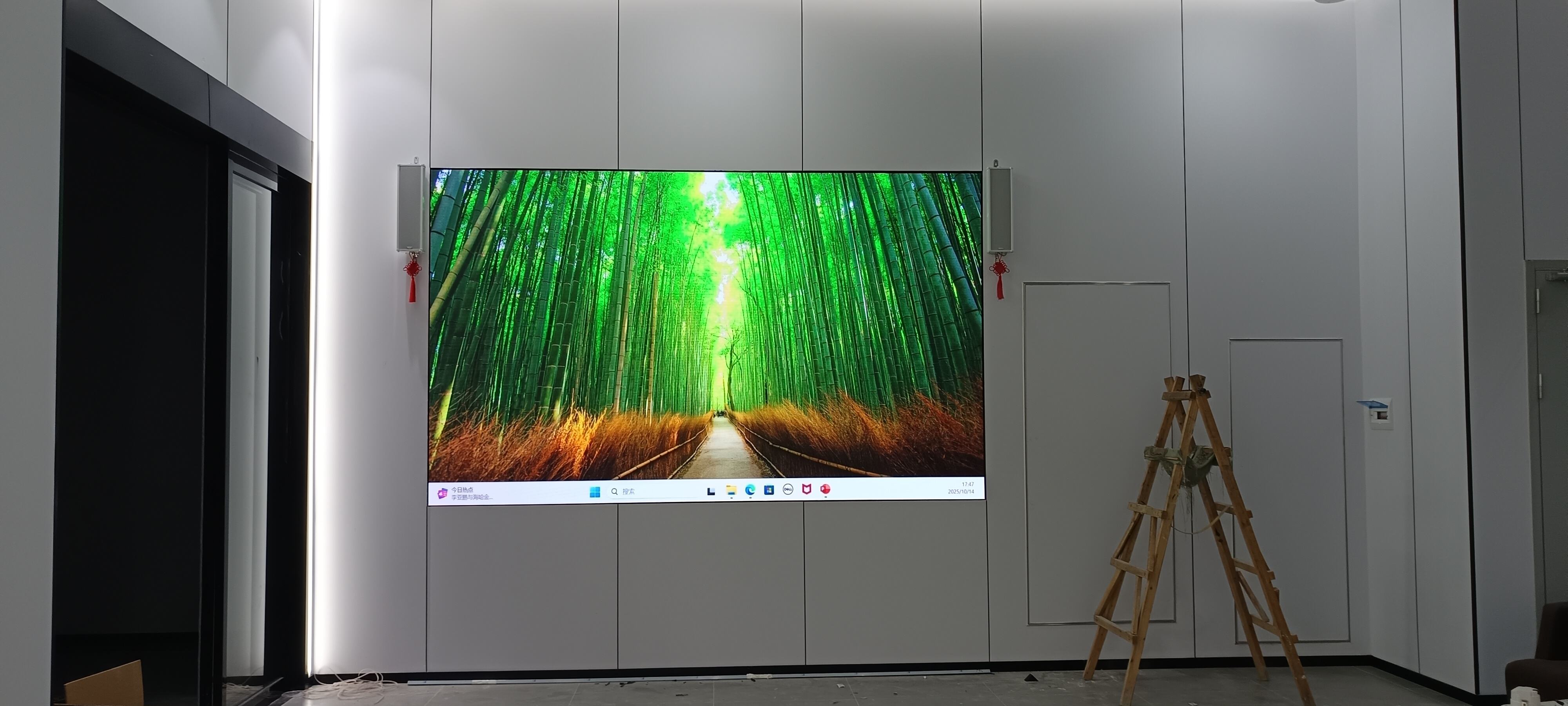 An ultrawide seamless LED display screen during installation in a corporate office, showing a bright green forest scene.