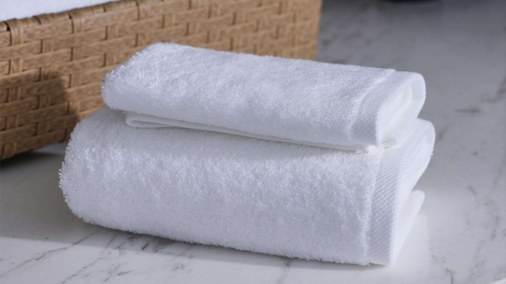 A professional stack of high-quality wholesale hotel towels presented elegantly on a marble surface next to a rattan basket..jpg
