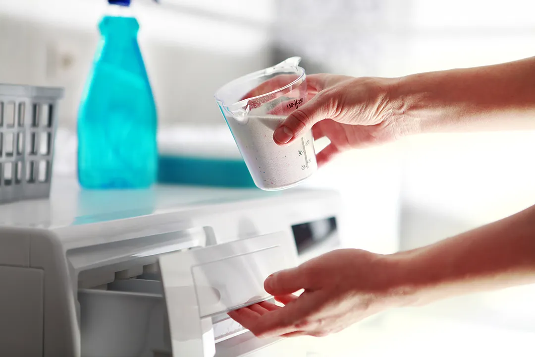 Hands adding professional-grade detergent into a commercial-style washing machine, showcasing best practices for hotel linen laundering.