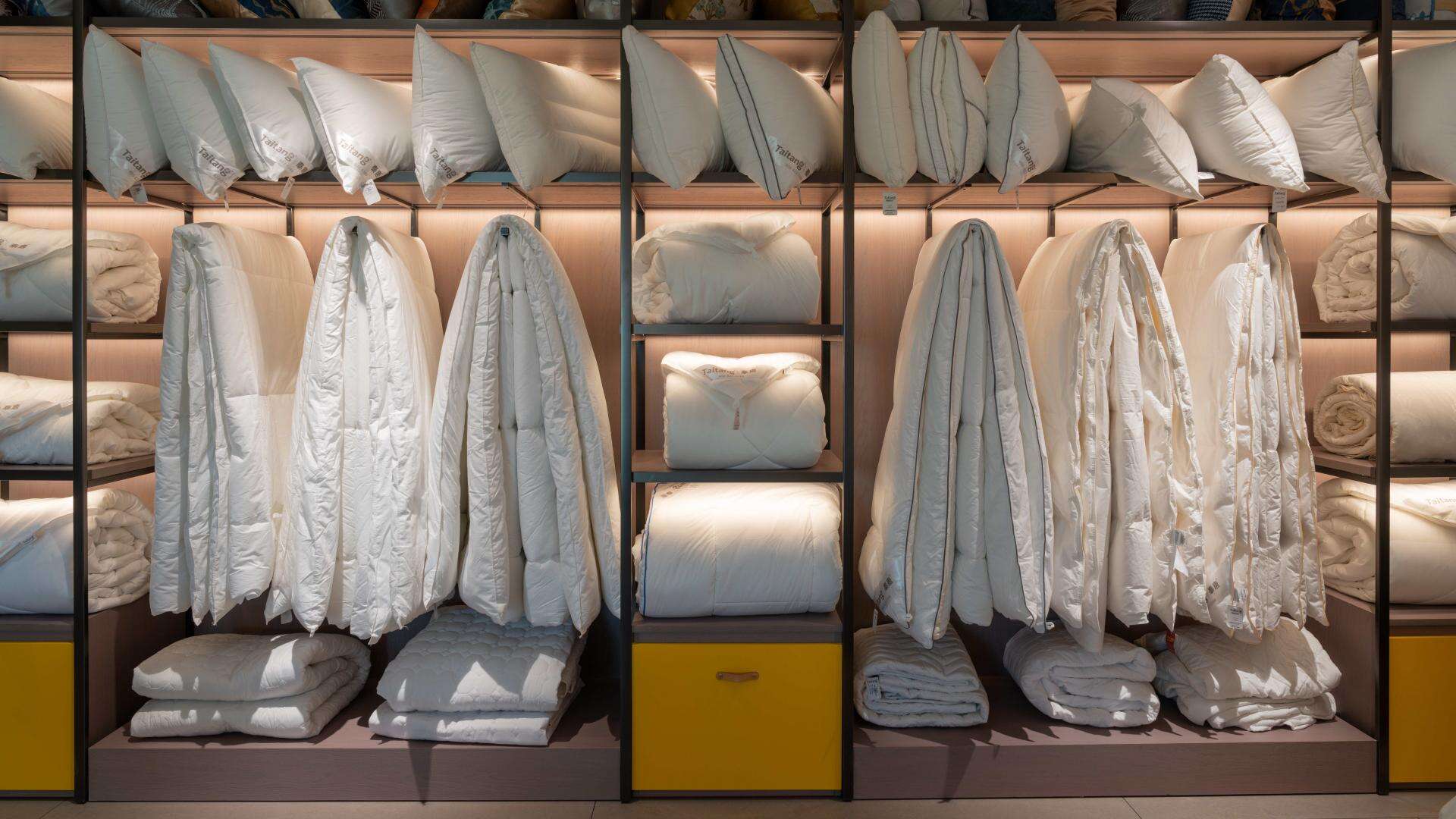 A professionally organized hotel linen storage closet displaying perfectly stacked and sorted wholesale white bedding sheets, duvets, and pillows.jpg