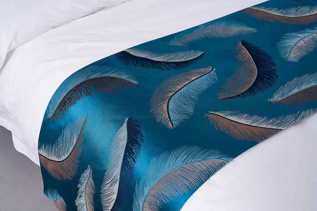 A detailed view of a decorative hotel bed runner with a stylish blue and gold feather motif, used to add style to hotel rooms.