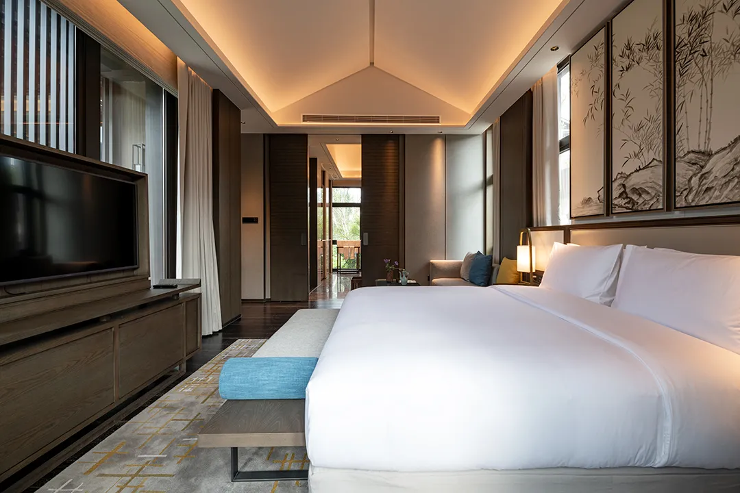 An inviting shot of a large, well-appointed modern luxury hotel room featuring a king-size bed with crisp, clean white bedding sets.