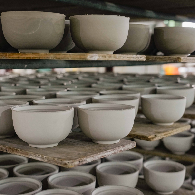 Rows of unfired ceramic greenware bowls organized on wooden drying racks inside a commercial porcelain tableware factory..jpg