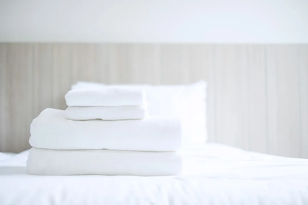 A tidy stack of high-quality, absorbent white cotton hotel towels and linens, ready for placement in a guestroom, supplied by Taitang.