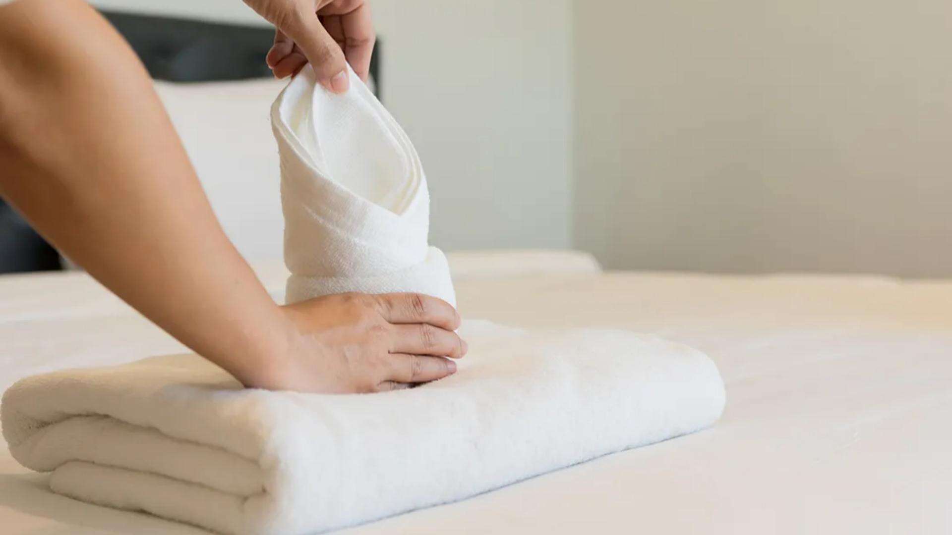 Housekeeping staff folding a premium white Taitang hotel bath towel on a guest room bed, emphasizing neatness and brand consistency..jpg