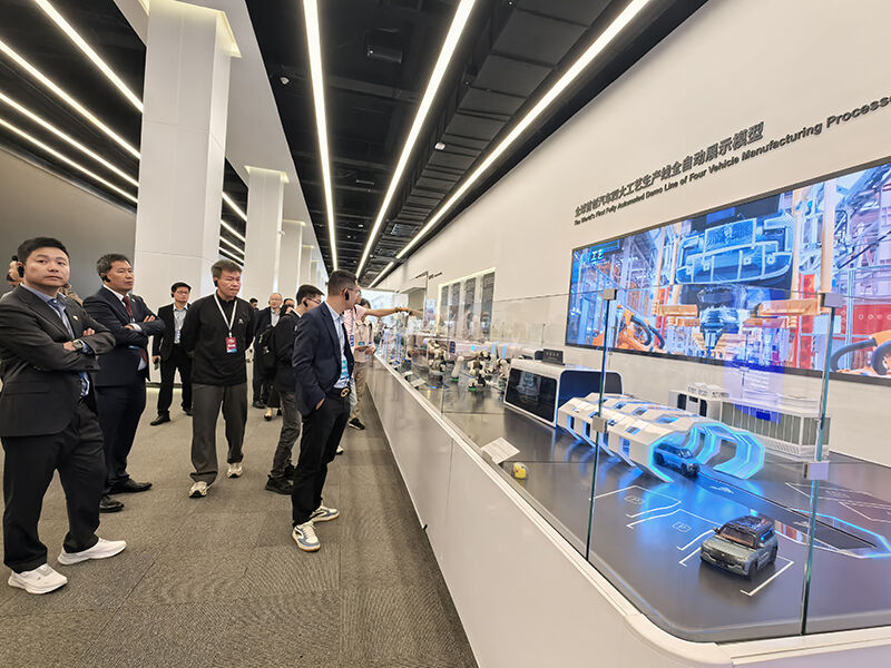 Visitors observing the smart safe production line demonstration model at BYD's exhibition hall, with a digital display screen introducing the manufacturing process.jpg