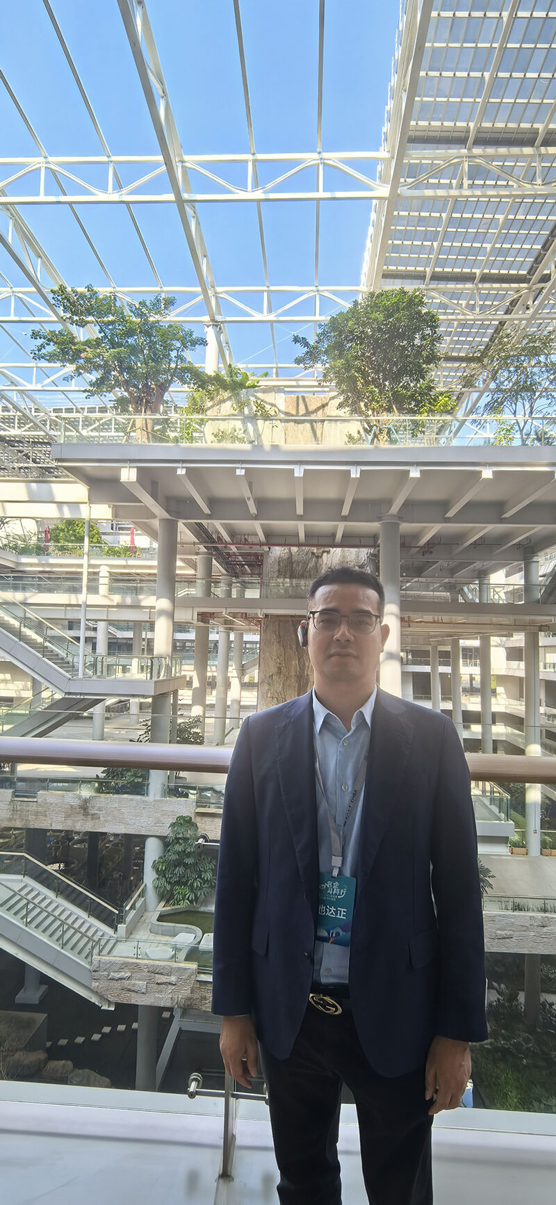 Dawson Chi standing in the indoor ecological atrium of BYD's facility, featuring multi-level architectural structures, glass roof and planted greenery.jpg