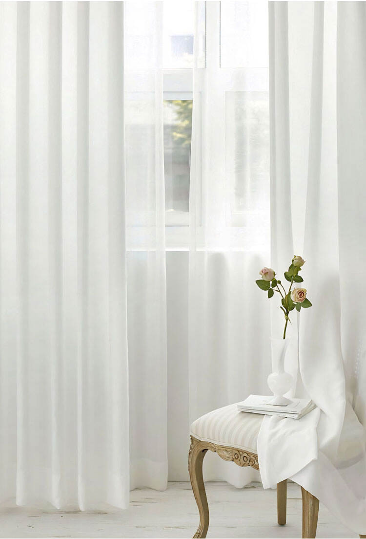 Sheer white curtains in a bright interior corner with chair and vase, creating soft light and an airy, elegant look.